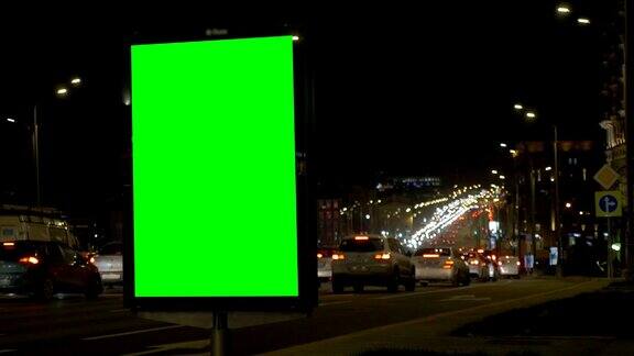 繁忙街道上的一个绿屏广告牌灯光和汽车的模糊背景