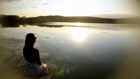 年轻女子在湖边的码头上休息透过她的太阳镜看日落美丽的秋日