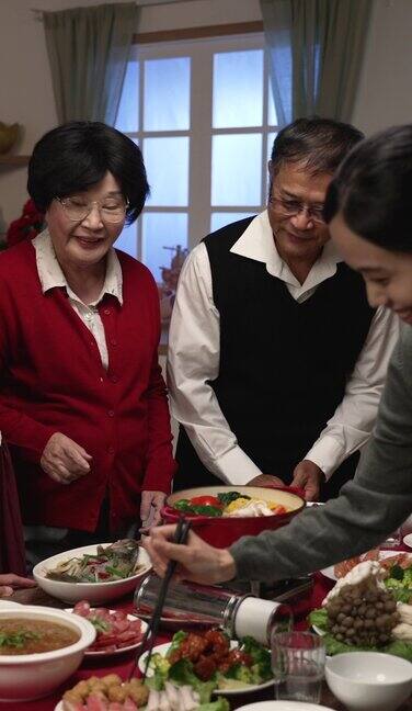 竖屏:中国农历除夕幸福的家庭成员围坐在餐桌旁亚洲父亲偷偷品尝年轻的母亲正在煮火锅