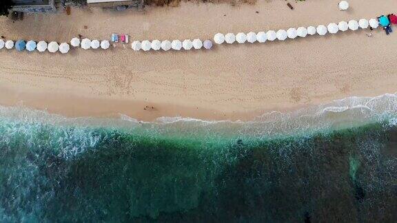 空中俯瞰海滩与太阳伞和绿松石海与波浪在巴厘岛