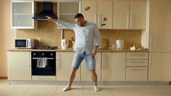 英俊的年轻有趣的男人在厨房跳舞在家里的早上和有乐趣的假期