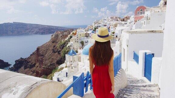 度假-旅游旅行妇女在伊亚圣托里尼希腊快乐的年轻女子走在楼梯上著名的蓝色圆顶教堂地标目的地美丽的女孩穿着红色的连衣裙在希腊的岛屿上游览
