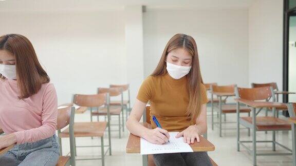一群女学生戴着面具坐在大学教室里学习和考试这是新常态