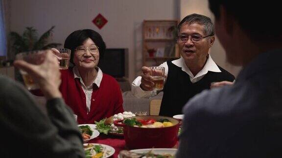 一位身着红色衣服的快乐老妇人在家中举行的团圆饭会上举起酒杯向家人敬酒庆贺农历新年