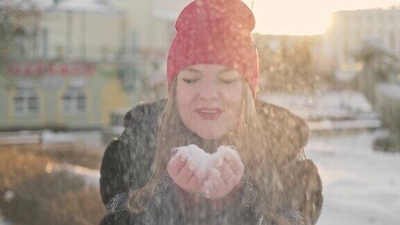 年轻女子吹雪花在日落女性正在户外吹雪