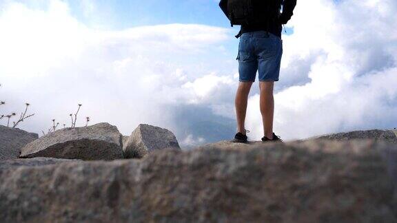 一个陌生的男性徒步旅行者背着背包站在山顶上欣赏美丽的风景背景是多云的天空旅行后视图慢动作低角度视图