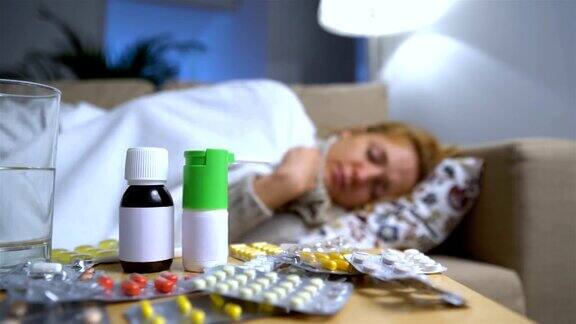沙发上一个生病的年轻女人面前的桌子上放着很多药片和药物