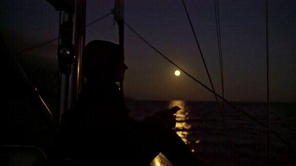 4K女人在帆船上放松背景是满月照在海上