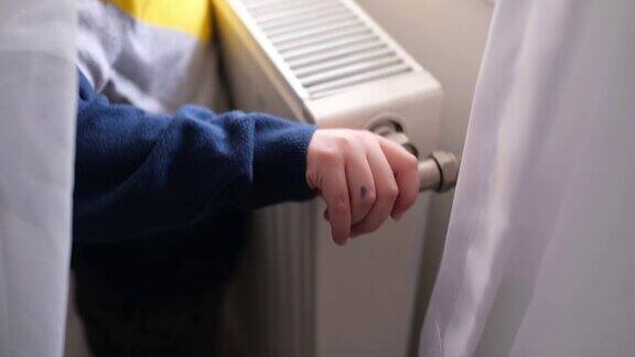 家用暖气片一个穿羊毛衫的孩子在暖炉旁暖手