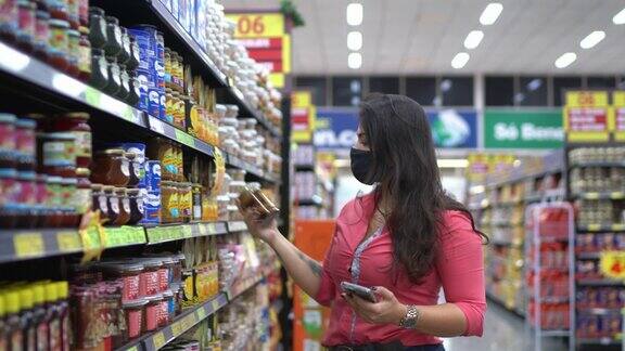 年轻女子戴着口罩在超市过道里检查商品