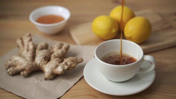 香茗倒进白色的杯子里木桌上放着姜、柠檬、蜂蜜和花草茶