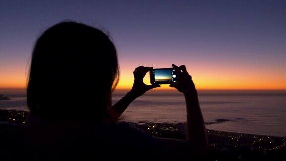 在海滩上用手机拍照的女人日落时的剪影