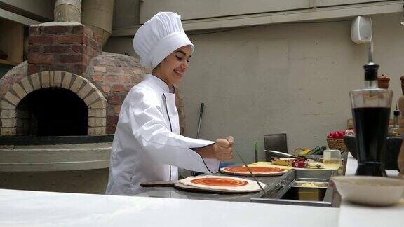 美丽的女厨师在一个餐馆做比萨饼添加番茄酱在面团上微笑