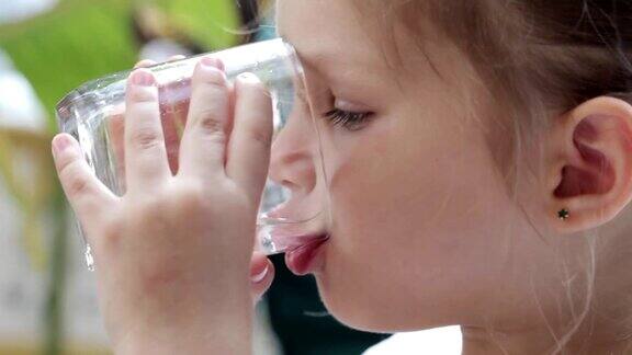 一个可爱的小女孩从杯子里喝纯净水的特写