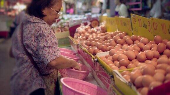 年长的亚洲妇女在农贸市场买鸡蛋