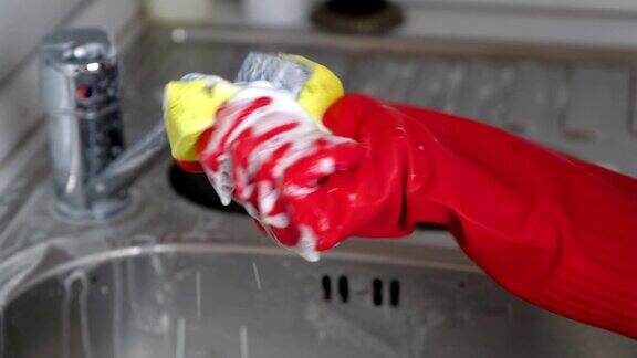 一位戴着红手套的妇女在厨房里用海绵清洗金属水龙头