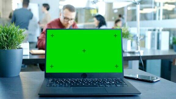 桌上的绿色模拟屏幕笔记本电脑在现代办公室工作的创造性年轻专业人员的背景