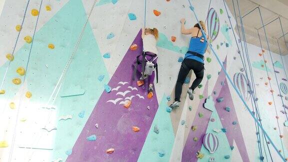 女性攀岩者在保护员的支持下在健身房室内攀岩的慢动作