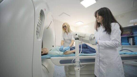 在现代医学诊所两名放射科医师插入静脉导管注射造影剂给正在接受CT或MRI扫描的女性患者病人躺在CT或MRI扫描床上在机器内移动