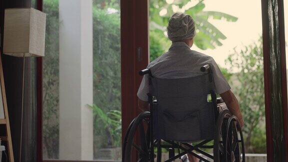 背部的亚洲癌症老人坐在轮椅上戴着一块大手帕以掩盖他的脱发化疗他正在看窗外的东西