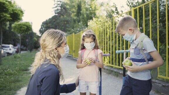 母亲戴着口罩拿着苹果在去学校的路上给了儿子和女儿