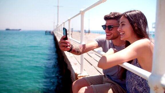 一对快乐的年轻潮人情侣在木栈桥上用智能手机视频聊天