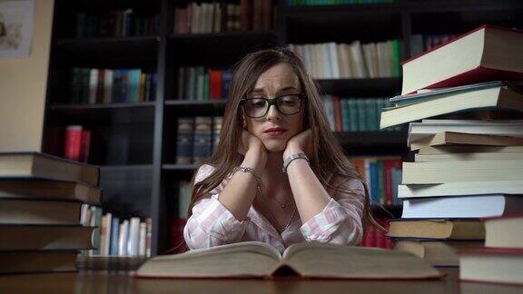 戴眼镜的女孩坐在图书馆的桌子旁学习