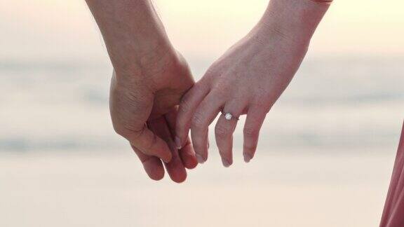 一对陌生的夫妇手牵着手戴着订婚戒指一男一女在沙滩上求婚后的特写