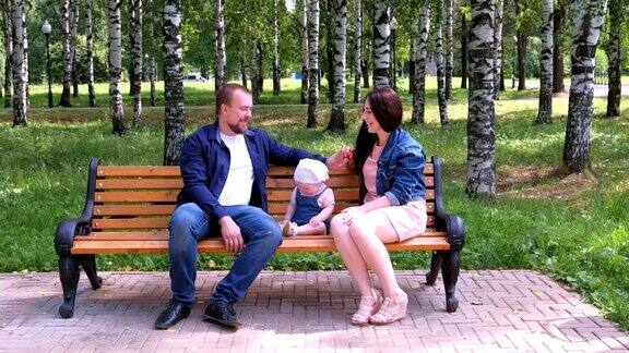 全家福妈妈爸爸和宝贝女儿坐在城市公园的长椅上聊天