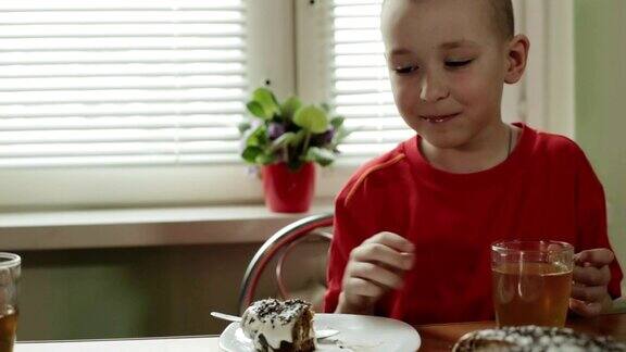 一个短头发的小男孩把一块蛋糕放进嘴里然后喝茶