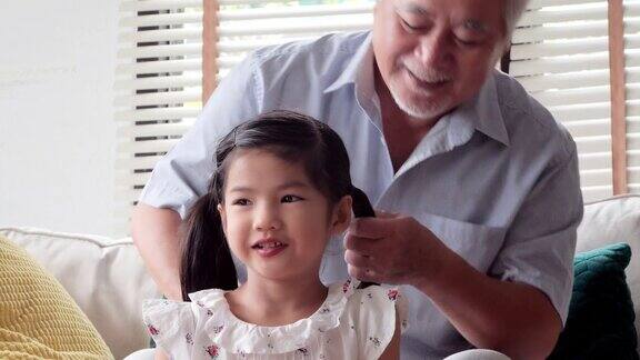 祖父掸去孙女的头发当爷爷给孙女梳头的时候可爱的小女孩在微笑幸福的家庭香港的家庭