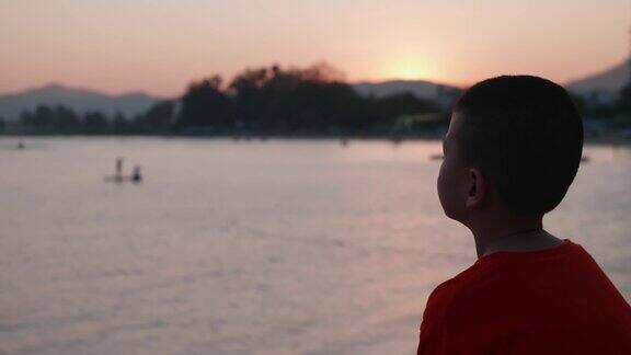一个孤独的亚洲男孩坐在海湾里寻找人们在夕阳下活动