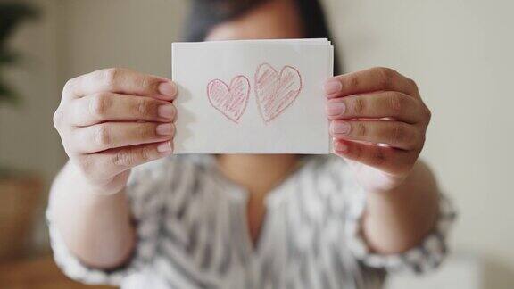 一名妇女展示了一张白纸上面用蜡笔画着红心