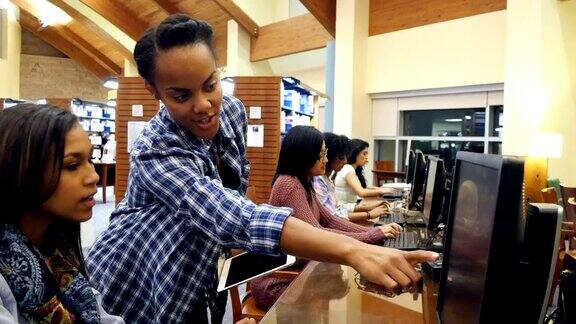 一位年轻的非裔美国女图书管理员在图书馆计算机实验室协助大学或高中学生