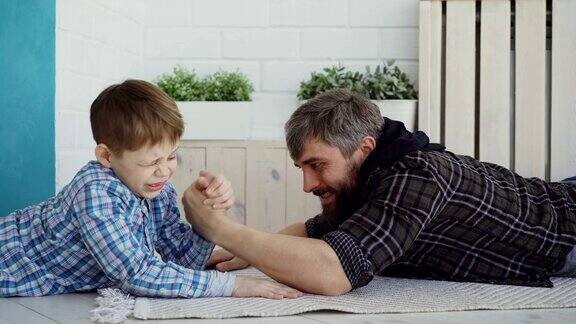 快乐的父亲正在教他的小儿子扳手腕给他看手的位置假装输了孩子对新的活动很感兴趣也很专注