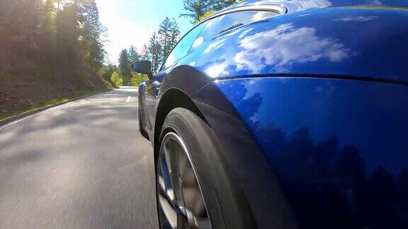 一辆蓝色的跑车行驶在空旷蜿蜒的乡间小路上被阳光照亮
