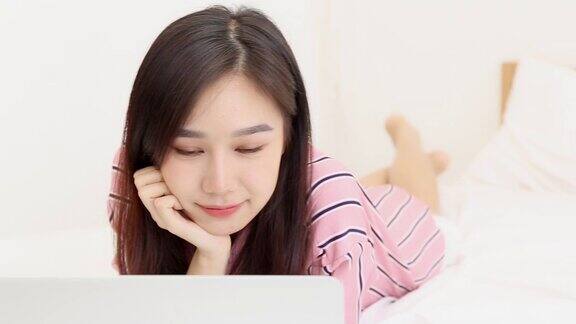 美丽的亚洲年轻女子躺在床上使用笔记本电脑在卧室休闲和放松自由职业者与女孩工作笔记本交流