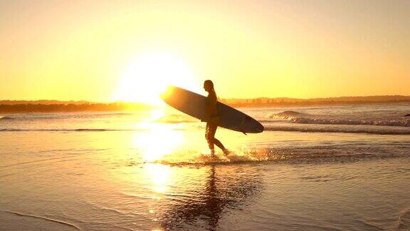 慢镜头:日落时分年轻的冲浪者女孩跑出大海溅起水花