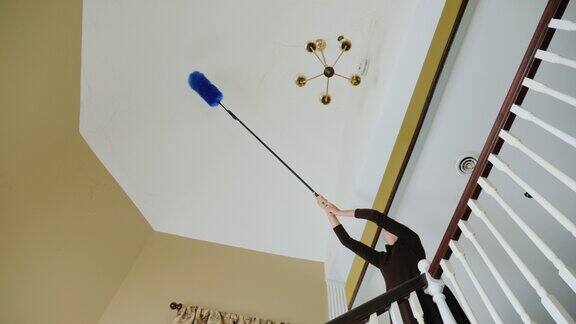 一个女人在清理枝形吊灯附近天花板上的蜘蛛网和杂物大房子清洁
