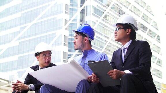 工程师小组在建筑工地顶部的露台上开会同事讨论老板和员工争吵在团队的对话戴上头盔拿纸上的计划