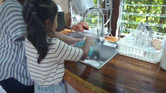 亚洲女孩和她的母亲一起在厨房里吃完饭后帮助清理和洗餐具