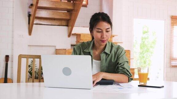 亚洲妇女在家厨房用笔记本电脑和计算器计算家庭预算