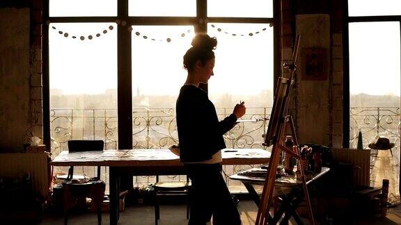 完全集中成熟的女性艺术家在她的20多岁正在画架上画画背后的阳光照亮了艺术工作室把它变成了激发创造力的环境