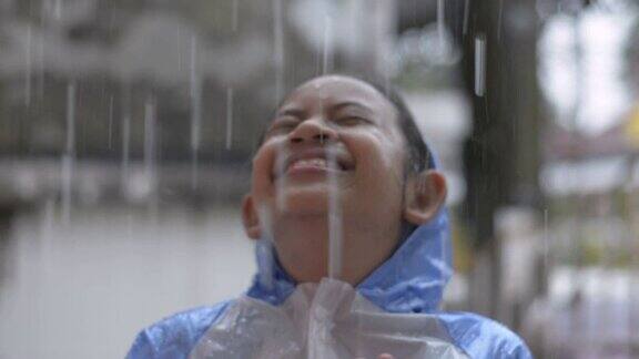 快乐的年轻亚洲女孩穿着蓝色雨衣喜欢在房前的雨中玩