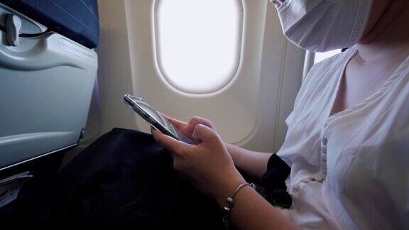 一名年轻女子戴着口罩坐在飞机座位上打电话