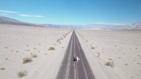 美国死亡谷新郎和新娘在空旷的沙漠路上奔跑