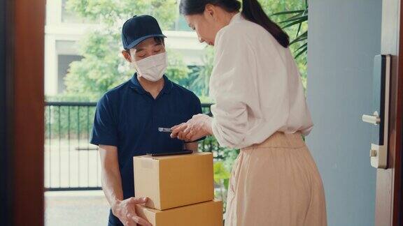 年轻的亚洲快递员戴着面具穿着蓝色海军制服携带箱子箱子敲门回家网上购物纸箱给女人在门口女士扫描二维码支付在家里的智能手机