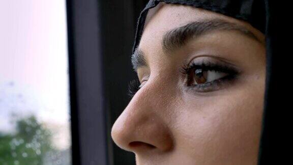 年轻的穆斯林妇女戴着头巾的眼睛在雨天的车窗里看着公交车天气概念交通概念城市概念梦想概念侧视