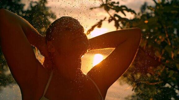 超级慢动作的女人在日落时在户外的海滩上洗她的头发