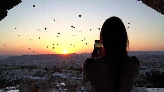 女游客在日出时用智能手机拍摄气球